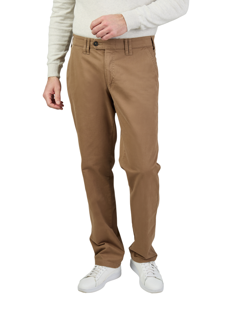 Herren in beige Chinos, getragen mit einer weißen langärmligen Strickjacke und weißen Sneakers, stehen vor einem neutralen Hintergrund.