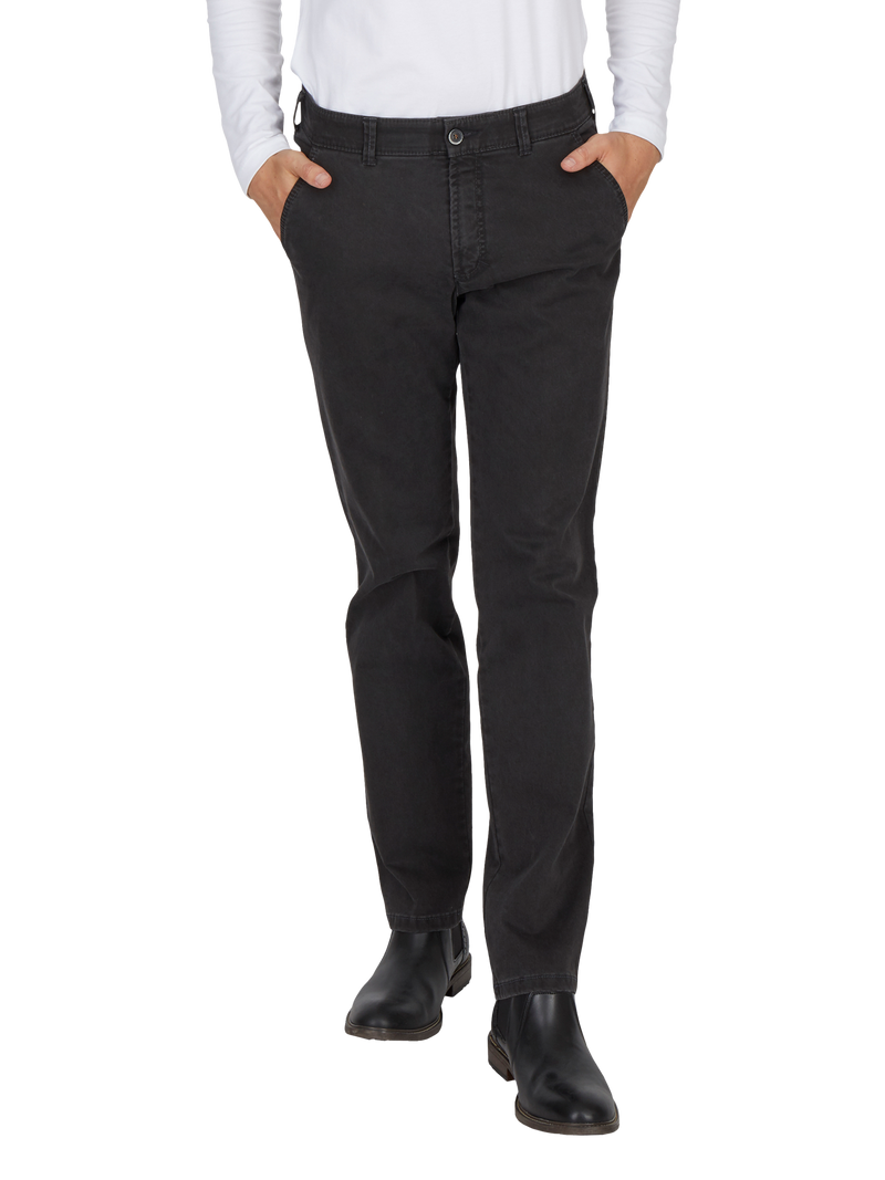 Ein Mensch trägt schwarze Jeans mit geradem Schnitt, ein weißes Hemd und schwarze Schuhe, die bis zu den Knöcheln reichen.