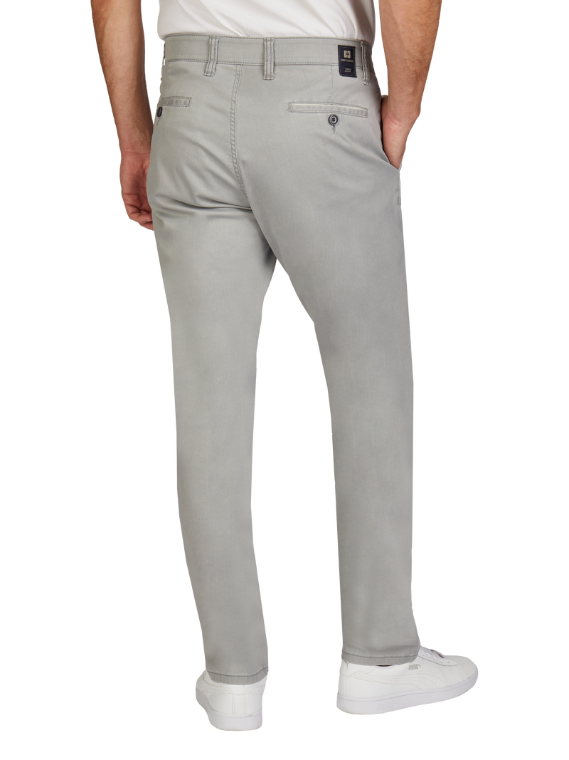 Ein Mann trägt hellgraue Chino-Hosen, die hinten einen Gehschlitz und zwei Taschen, eine davon mit Knopf, haben. Er steht mit den Händen in den Taschen, trägt weiße Sneakers und ein weißes T-Shirt.