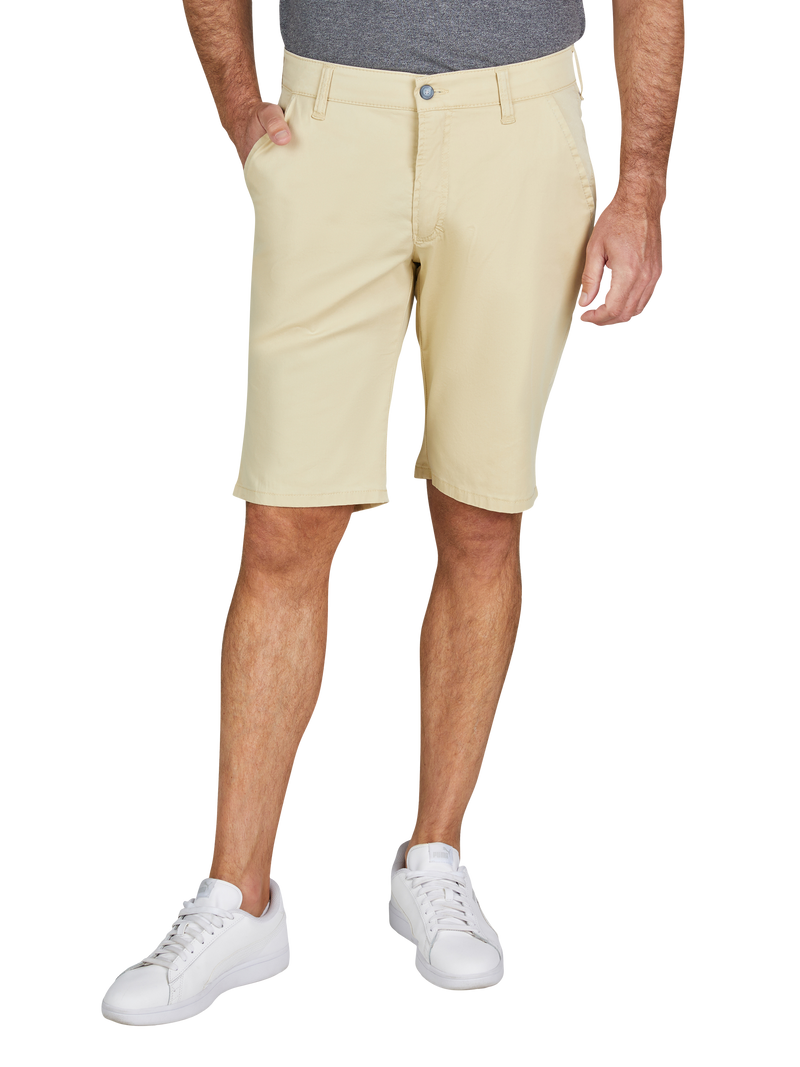 Mann trägt hellgelbe Kniebund-Shorts, grau T-Shirt, weiße Sneaker, steht mit einer Hand in der Tasche, die andere Hand hängt seitlich.