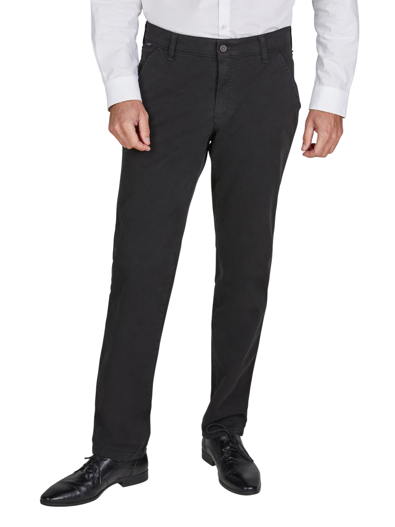 Ein Mann trägt eine weiße, langarmige Hemdseite und schwarze Chino-Hosen mit Gürtelschlaufen. Er trägt schwarze Schuhe und steht mit den Händen an den Seiten.