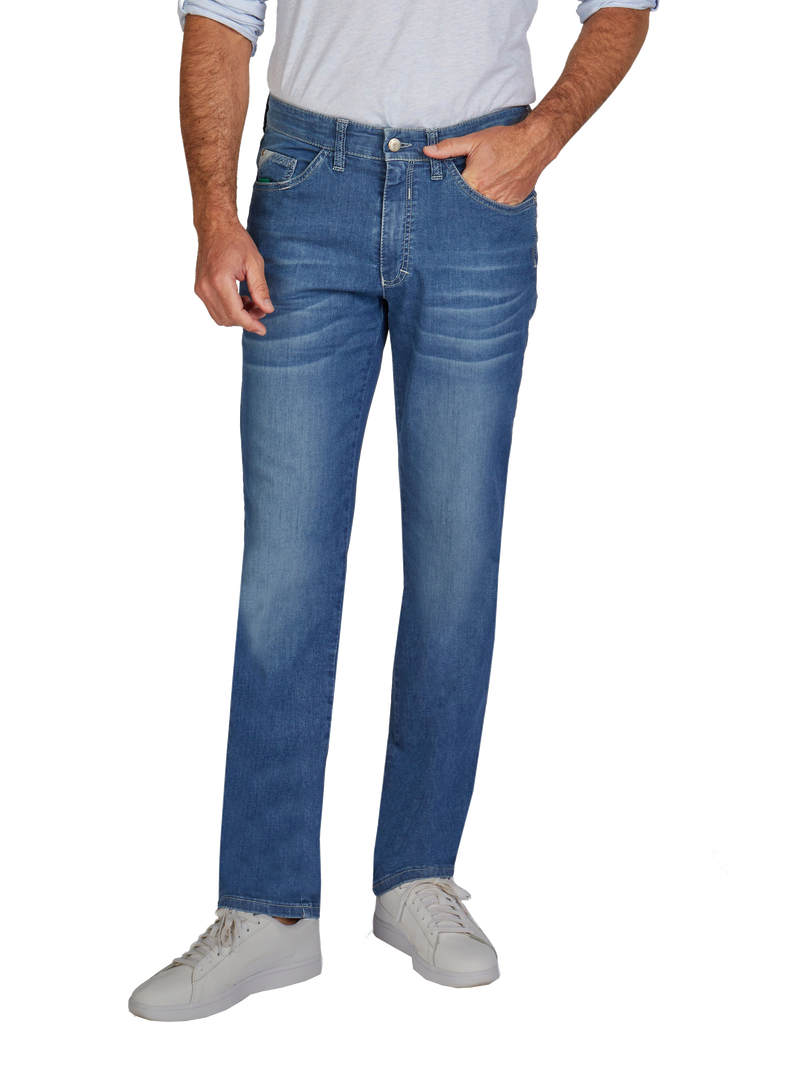 Ein Mann trägt eine graue Hemd, blaue Jeans und weiße Sneakers. Seine linke Hand steckt in der Hosentasche, während die rechte Hand neben seinem Bein hängt.