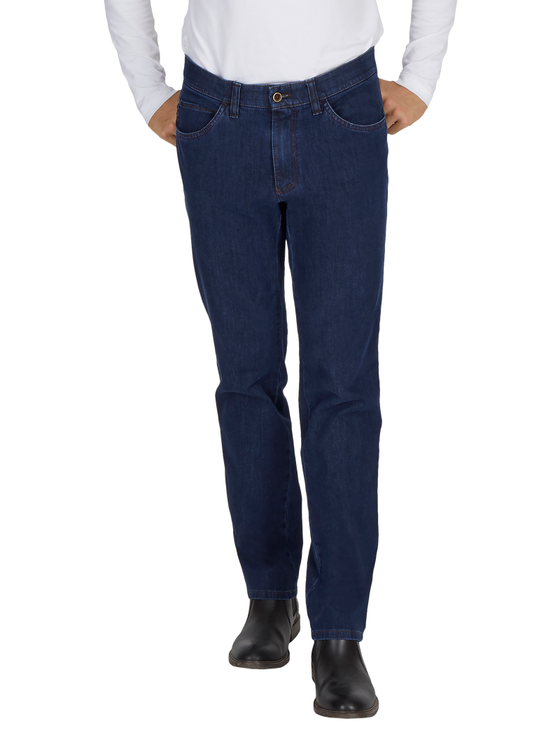 Blick auf eine Person, die dunkelblaue Jeans trägt, die an der Taille sitzen, mit geradem Schnitt, und ihre Hände in den Taschen haben. Die Person trägt dazu schwarze Stiefel und ein weißes Oberteil.