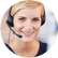 Nahaufnahme einer jungen Frau mit blonden Haaren, die freundlich lächelt und einen schwarzen Headset mit Mikrofon trägt, während sie sich offensichtlich in einem Kundenservice- oder Support-Umfeld befindet.