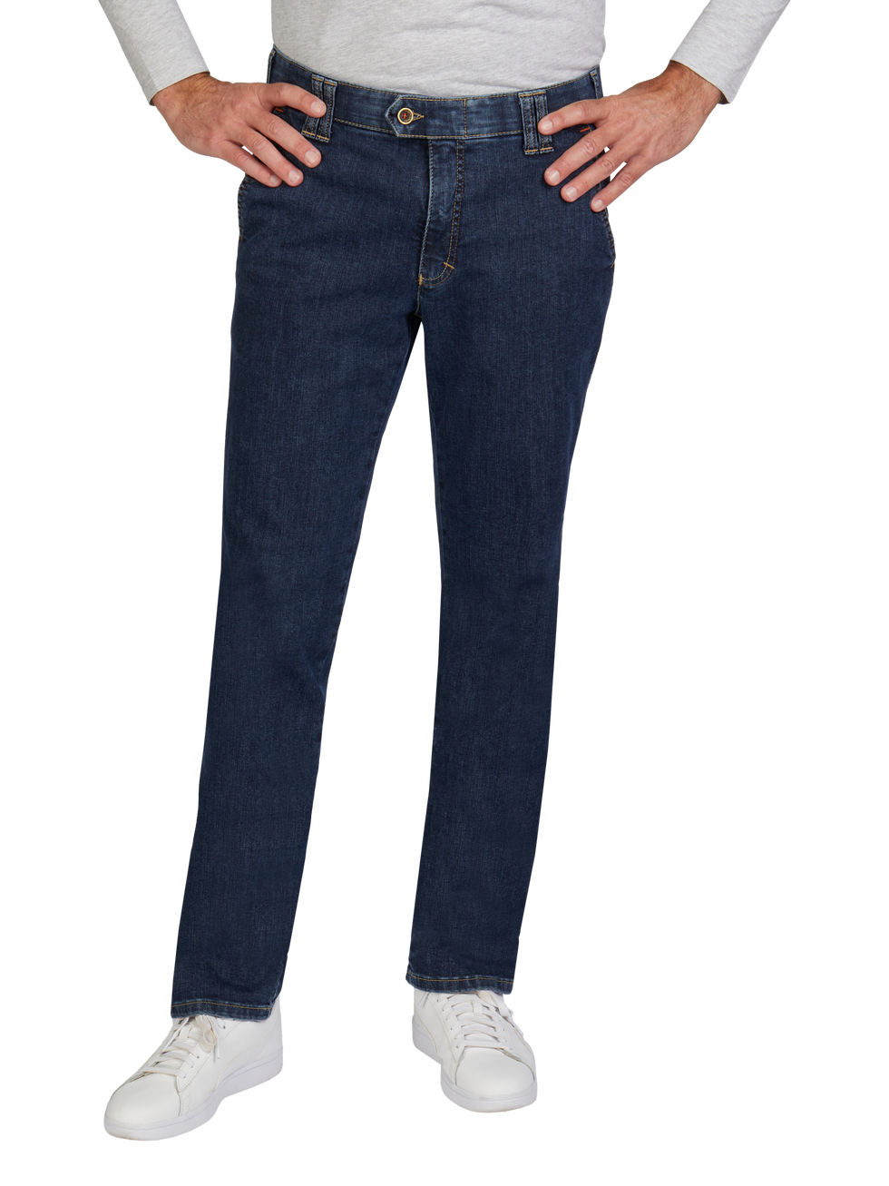 Nahaufnahme einer Person, die dunkle Blue Jeans trägt, die an den Hüften und Beinen gut sitzen. Die Person hat die Hände auf die Hüften gelegt, trägt weiße Sneakers und ein hellgraues Langarmshirt. Der Hintergrund ist transparent.